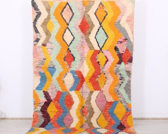 May include: A colorful Moroccan rug with a geometric diamond pattern in shades of orange, yellow, blue, pink, and green. The rug has a fringe border.