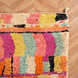May include: A vibrant rug with a geometric design. The rug displays a variety of colours, including pink, yellow, orange, and black. The rug is made from a thick, woven material.