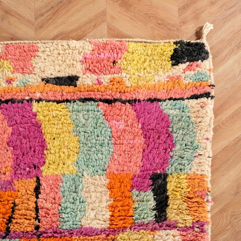 May include: A vibrant rug with a geometric design. The rug displays a variety of colours, including pink, yellow, orange, and black. The rug is made from a thick, woven material.
