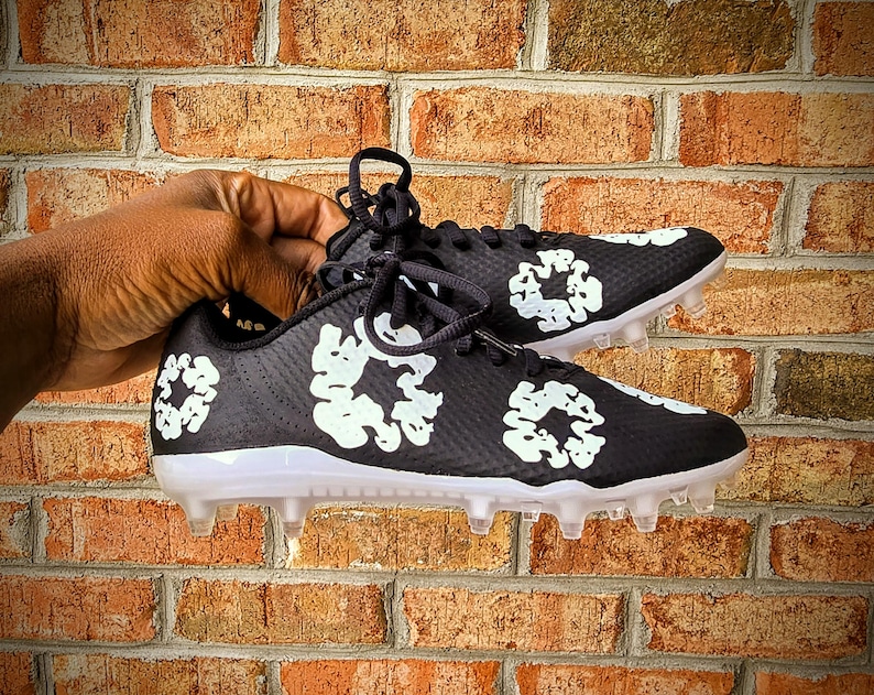 May include: Black and white soccer cleats with a floral design. The cleats have a black base with white floral patterns and clear studs on the sole. The laces are black.