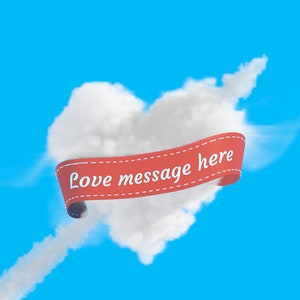 Puede incluir: Una cinta roja con el texto "Love message here" est&aacute; envuelta alrededor de una nube con forma de coraz&oacute;n contra un cielo azul.