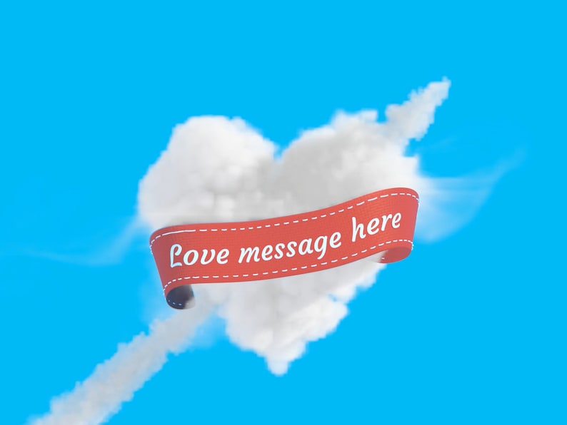 Puede incluir: Una cinta roja con el texto "Love message here" est&aacute; envuelta alrededor de una nube con forma de coraz&oacute;n contra un cielo azul.