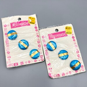 May include: Two packs of blue and gold buttons with the word "Nouveauté" printed on them. The buttons are packaged on white cards with pink and white snowflake designs.