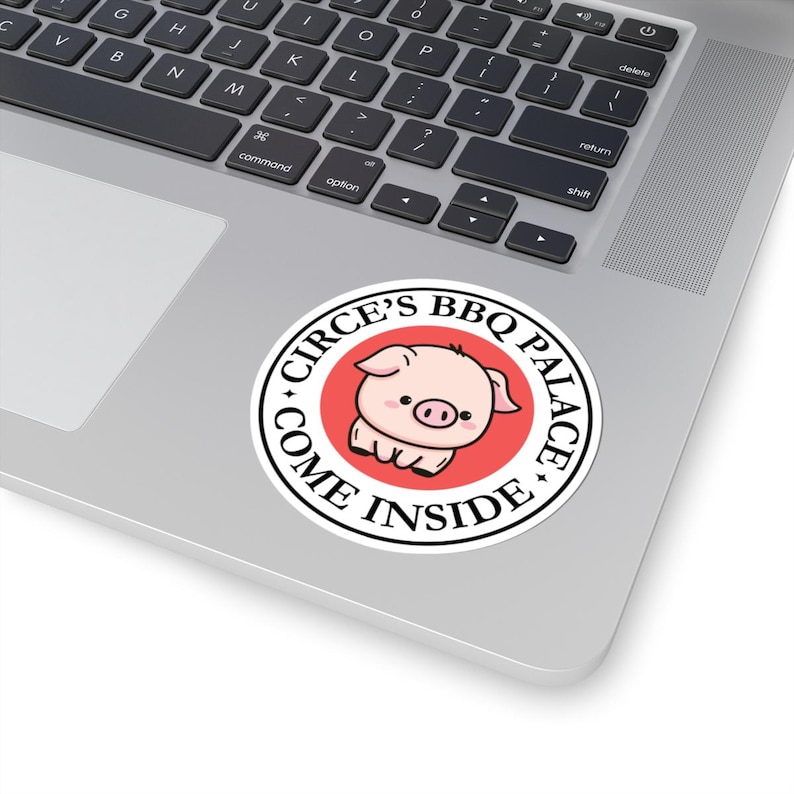 May include: A round sticker with the text "CIRCE'S BBQ PALACE COME INSIDE" encircling a cartoon pig on a red background. The sticker is white with black text and is placed on a laptop.