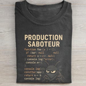 May include: Dark gray t-shirt with the text "PRODUCTION SABOTEUR" in tan. Below the text is computer code and a cartoon insect wearing a bandana. The shirt is folded.