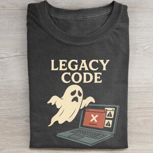 May include: Dark gray t-shirt with the words "LEGACY CODE" in a cream color. A cartoon ghost hovers over a laptop with an error message. The laptop is gray with a red error window.