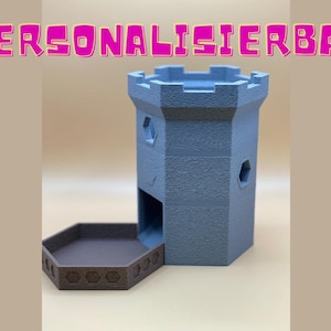 Op de afbeelding: Een blauwe torenvormige dobbelsteenroller met een bruine lade. De toren heeft zeshoekige ramen en een getextureerd oppervlak. Het woord "PERSONALISIERBAR" staat in roze letters boven de toren.