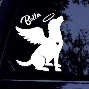 May include: White vinyl decal of a dog with angel wings and a halo. The dog is facing right and has a heart on its chest. The text "Bella" is above the dog.