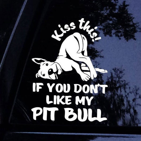 May include: A white vinyl decal featuring a graphic of a dog in a playful pose with the text "Kiss this!" above and "IF YOU DON'T LIKE MY PIT BULL" below. The design is applied to a dark glass surface, showing the dog looking back over its shoulder.