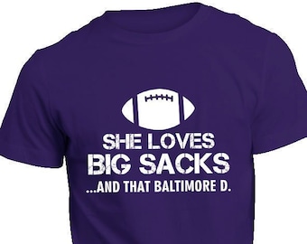May include: Purple t-shirt with a white football graphic and the text "She loves big sacks...and that Baltimore D."