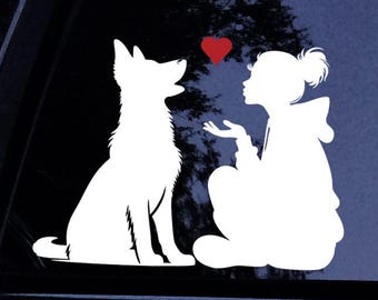 May include: White vinyl decal featuring a silhouette of a dog looking up at a red heart. A person is seated, blowing a kiss towards the heart. The decal is designed to be applied to a car window.
