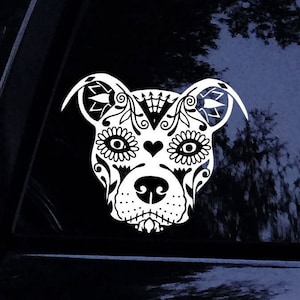 May include: A white decal of a dog's face, featuring intricate floral and heart designs, resembling a sugar skull. The dog's face is centered, with detailed patterns around the eyes, ears, and nose, creating a decorative and artistic appearance.