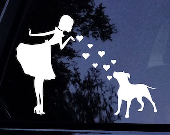 Puede incluir: Una calcomanía de vinilo blanco que representa a una mujer soplando besos en forma de corazón hacia un perro. El perro mira los corazones. La calcomanía está diseñada para aplicarse en la ventana de un coche o superficie similar.
