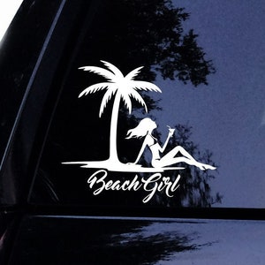 Puede incluir: Calcomanía de vinilo blanco con una palmera y la silueta de una persona relajándose en una playa, sosteniendo una bebida. El texto "Beach Girl" está escrito en cursiva debajo.