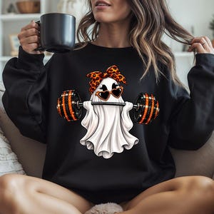 Könnte beinhalten: Ein schwarzes Langarm-Sweatshirt mit einer Grafik eines weißen Geistes, der ein Stirnband mit Leopardenmuster und herzförmige Sonnenbrillen trägt, während er eine Langhantel mit orangefarbenen und schwarzen Gewichten hebt.