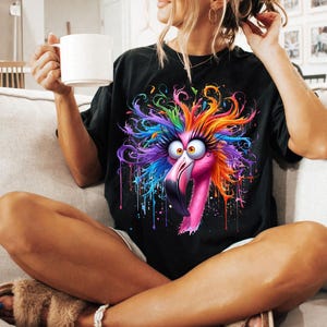 May include: A black t-shirt with a colorful graphic of a flamingo with rainbow feathers and paint splatters.