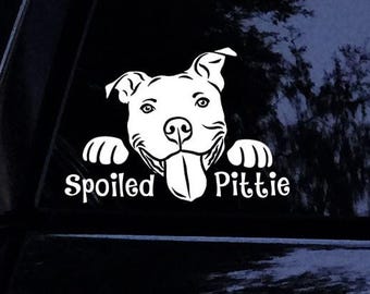 Pode incluir: Um autocolante de vinil branco com um cão pitbull de desenho animado com as patas dianteiras apoiadas numa superfície, a língua de fora e o texto "Spoiled Pittie" escrito num tipo de letra estilizado por baixo da cabeça do cão.