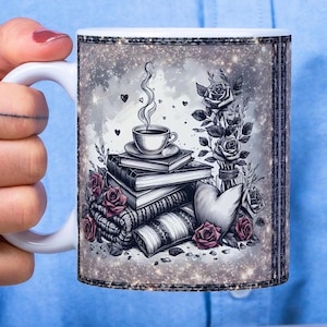 May include: White ceramic mug featuring a black and white illustration of a coffee cup atop a stack of books, roses, and a heart. The mug has a glittery border and is held by a person wearing a blue shirt.