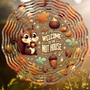 May include: A decorative wind spinner featuring a cartoon squirrel holding an acorn, surrounded by leaves and acorns. The text "WELCOME TO THE NUT HOUSE" is displayed in the center. The design has a brown and gold color scheme.