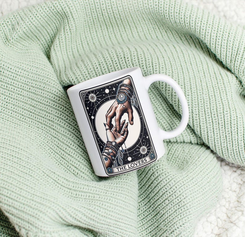 Pu&ograve; includere: Tazza in ceramica bianca con un'illustrazione in bianco e nero di due mani che si tengono. L'illustrazione &egrave; circondata da un cerchio di stelle e il testo "THE LOVERS" &egrave; stampato sotto l'immagine.