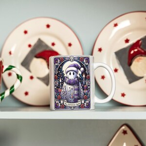 May include: White ceramic mug with a colorful illustration of a ghost wearing a purple scarf and hat. The text "The Christmas Spirit" is printed on the mug.