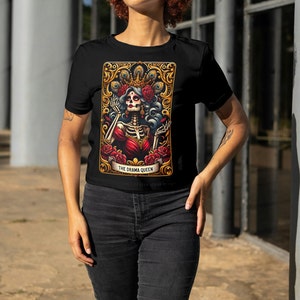May include: Black t-shirt with a graphic print of a skeleton woman wearing a crown and red dress. The graphic is surrounded by a gold frame and the text "THE DRAMA QUEEN".