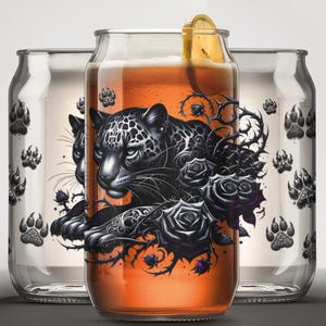 May include: Three glass beverage containers with black and white illustrations of a jaguar, roses, and thorns. The center container is filled with a dark amber liquid.