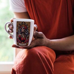May include: White ceramic mug with a colorful illustration of a skeleton queen with a crown and a red dress. The mug has the text "The Drunk Queen" printed on the bottom.