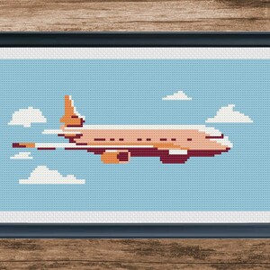 May include: A cross-stitch pattern of an orange airplane flying in a blue sky with white clouds.