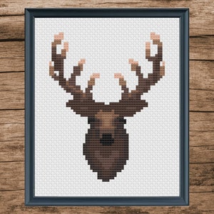 May include: A framed cross-stitch design of a brown deer head with large antlers. The deer is on a white background.