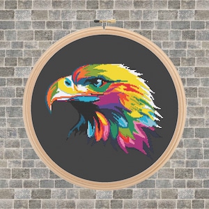 Może przedstawiać: Kolorowy, abstrakcyjny wzór haftu krzyżykowego przedstawiający głowę orła. Orzeł jest przedstawiony w różnych jasnych kolorach, w tym żółtym, czerwonym, niebieskim, zielonym i fioletowym. Tło jest ciemnoszare.