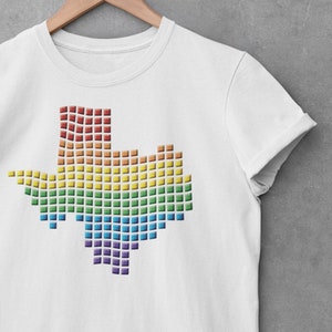 May include: White t-shirt with a rainbow-colored outline of the state of Texas. The outline is made up of small squares.
