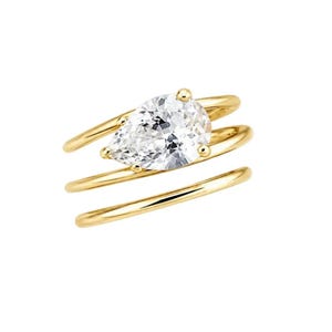 Könnte beinhalten: Ein Goldring mit einem birnenförmigen, klaren Edelstein auf einer mehrsträngigen Ringschiene. Die Schiene besteht aus drei glatten, polierten Golddrähten, die sich um den Finger winden, wobei der facettierte Stein oben durch kleine Krallen gehalten wird.