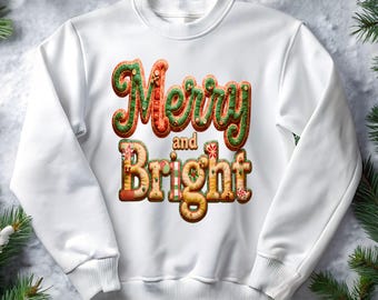 Puede incluir: Sudadera blanca con las palabras "Merry and Bright" en una fuente festiva de estilo pan de jengibre. El texto está en tonos de rojo, verde y marrón, con detalles decorativos. La sudadera es de cuello redondo.