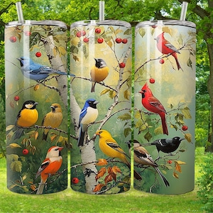 Puede incluir: Tres vasos de acero inoxidable con diseños de pájaros coloridos. Los vasos presentan un abedul blanco con bayas rojas, pájaros azules, amarillos y rojos, y hojas verdes.