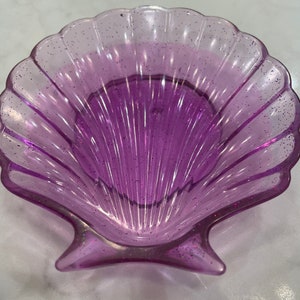 May include: A purple iridescent seashell-shaped dish with glitter embedded in the plastic.