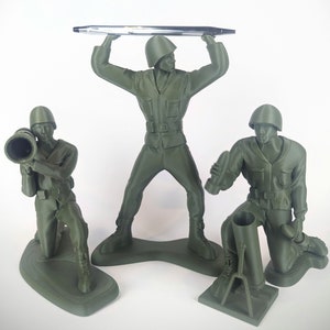 Peut inclure: Trois soldats en plastique vert, l'un tenant un stylo, l'autre un bazooka et le dernier un mortier. Les soldats sont tous dans des poses diff&eacute;rentes et se tiennent sur une surface blanche.