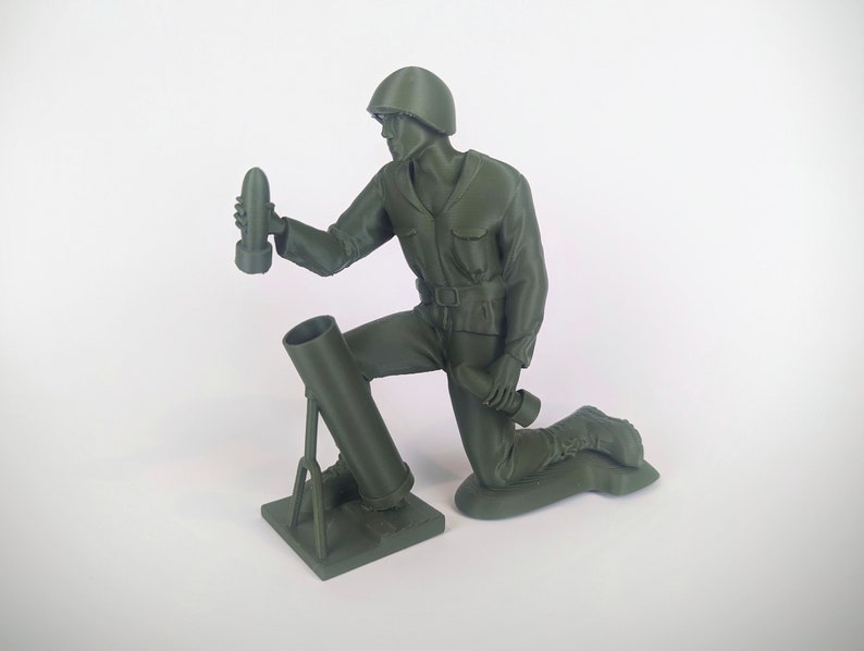 Peut inclure: Une figurine de soldat en plastique vert agenouill&eacute; tenant un obus de mortier. Le soldat porte un casque et a un fusil en bandouli&egrave;re. Le mortier est mont&eacute; sur un tr&eacute;pied.