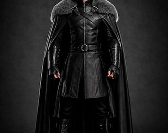 May include: A black leather-look long coat featuring a high collar, a waist belt with a silver buckle, and a floor-length cape with a thick grey faux fur collar. The outfit includes matching black fingerless gauntlets and tall black boots.