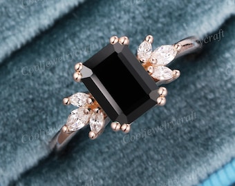 Könnte beinhalten: Ein schwarzer Smaragdschliff-Verlobungsring mit einer Roségold-Schiene und Diamant-Akzenten. Der Ring ist in einem floralen Design mit kleinen Diamanten auf jeder Seite des Mittelstücks gefasst.