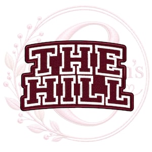 May include: A maroon embroidered patch featuring the text THE HILL in a bold, white-outlined block font. The design has a curved top and bottom edge, with a textured fabric appearance and a thick, stitched border surrounding the lettering.