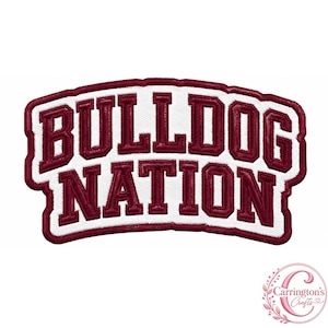 Puede incluir: Un parche bordado que presenta el texto BULLDOG NATION en letras de bloque de color granate oscuro con un contorno blanco. El parche tiene una forma curva y un fondo blanco, con un borde granate que sigue el contorno de las letras.