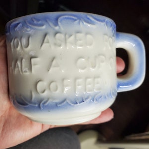 May include: White ceramic coffee mug with blue trim and the text "You asked for half a cup of coffee" embossed on the front.