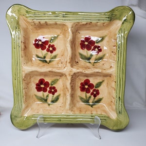 May include: A square ceramic serving dish with four sections. Each section has a floral design with red flowers and green leaves on a beige background. The dish has a green rim with a raised design.