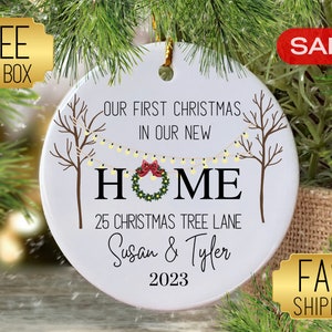 May include: White ceramic Christmas ornament with the text "Our First Christmas in Our New Home" and "25 Christmas Tree Lane". The ornament also includes the names "Susan & Tyler" and the year "2023".