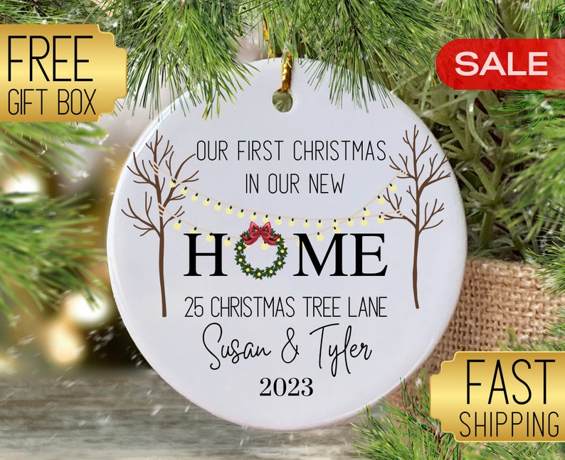Puede incluir: Adorno navide&ntilde;o de cer&aacute;mica blanca con el texto "Nuestra primera Navidad en nuestro nuevo hogar" y "25 Christmas Tree Lane". El adorno tambi&eacute;n incluye los nombres "Susan & Tyler" y el a&ntilde;o "2023".