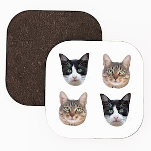 May include: Four different cat faces are shown on a white square coaster. The cats are all looking at the camera. Two of the cats are black and white, and two of the cats are tabby.