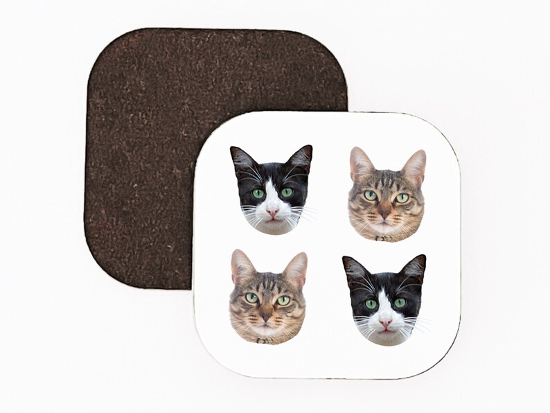 May include: Four different cat faces are shown on a white square coaster. The cats are all looking at the camera. Two of the cats are black and white, and two of the cats are tabby.