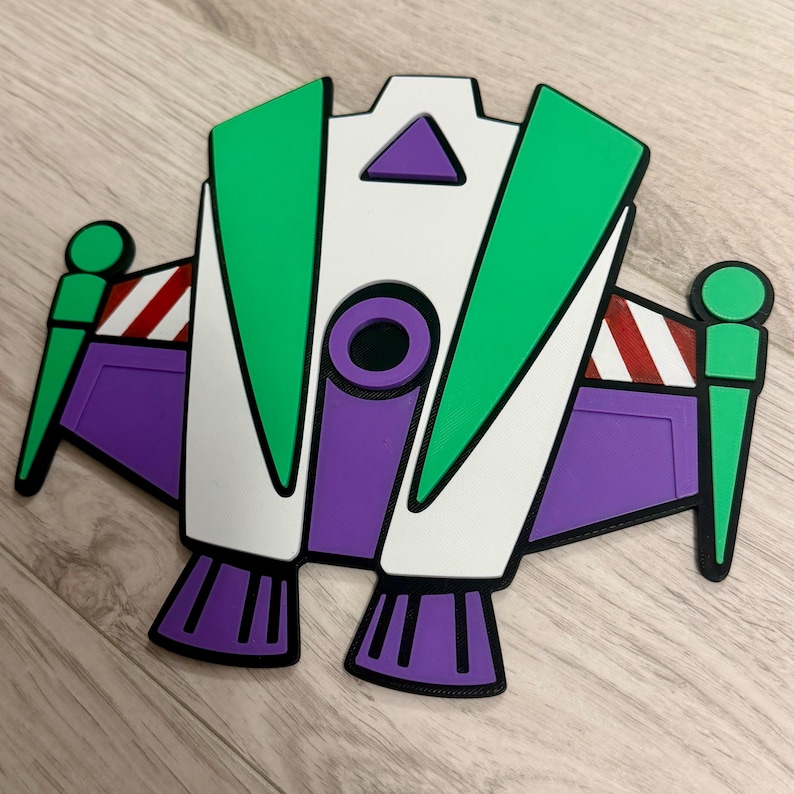 May include: A colorful, stylized depiction of a space shuttle, featuring green, white, purple, and black accents. The design includes wings, a central body, and thrusters, with red and white striped details. The overall shape is reminiscent of a cartoon character.