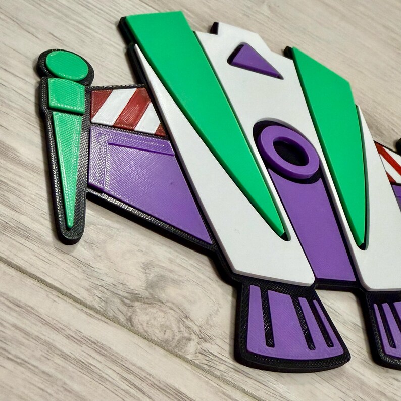 May include: A colorful 3D-printed toy, featuring a design with green, white, purple, and red accents. The toy has a distinct shape with geometric elements and a black outline. The design is reminiscent of a space ranger.